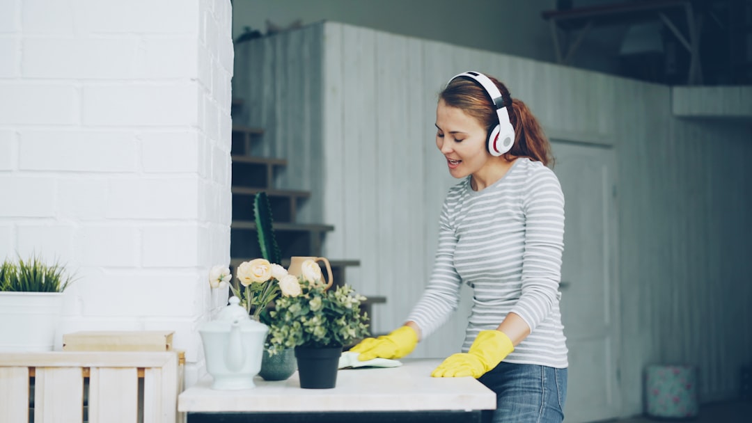 about-01 Good-looking girl is dusting table at home and listening to pop music through headphones, singing and dancing with happy face. Millennials, household and interior concept.